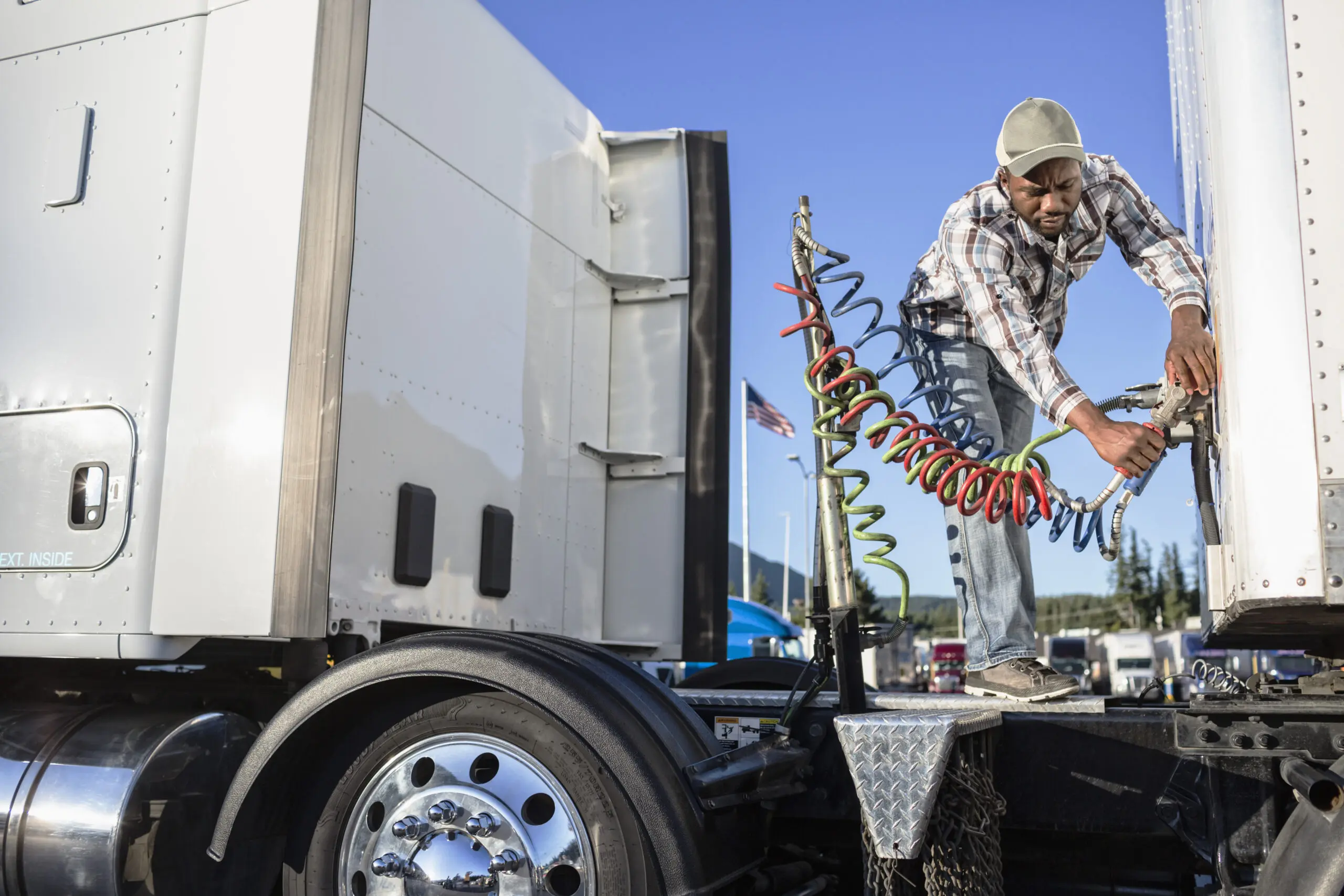 Black man truck driver attaching power cables from truck tractor to trailer at a truck stop